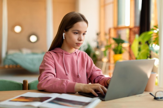 Adolescente concentrada en la educación en el hogar usando una computadora portátil en su habitación escribiendo en el teclado y mirando la pantalla de la computadora