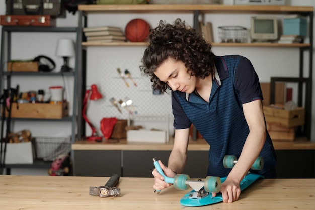 Adolescente contemporáneo montando ruedas de monopatín por mesa en garaje