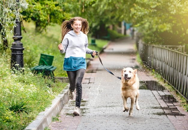 Adolescente corriendo con perro golden retriever en el parque después de la lluvia