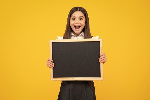 Foto adolescente criança segurando quadro preto isolado em um fundo amarelo rosto excitado emoções alegres de adolescente
