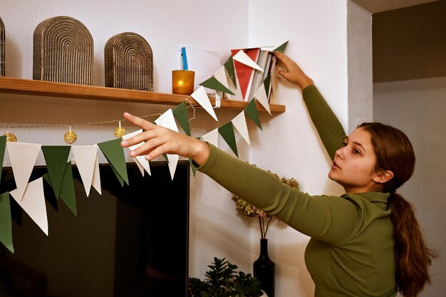 Foto una adolescente cuelga banderas de papel navideñas festivas en su apartamento