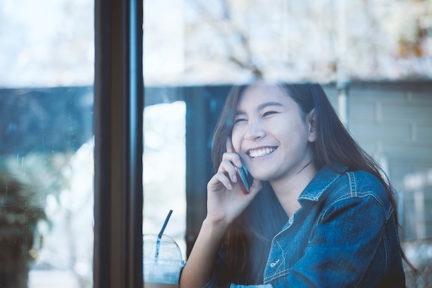 Adolescente da Ásia sentado sozinho usando o celular com sorria no café.