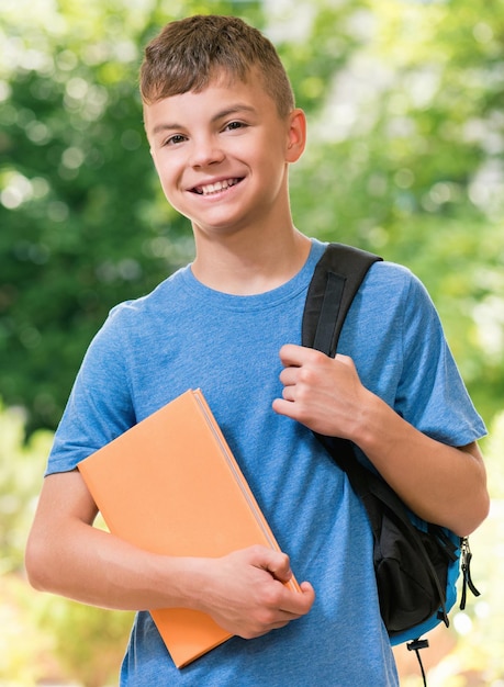 Foto adolescente de 12-14 anos com saco escolar e livro posando ao ar livre