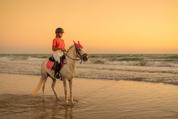 Adolescente de 14 anos monta seu cavalo branco à beira-mar vestindo roupas rosa combinando