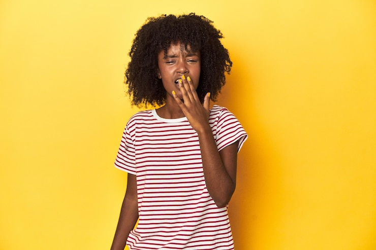 Foto adolescente de camiseta listrada vermelha com fundo de estúdio amarelo bocejando mostrando um gesto cansado
