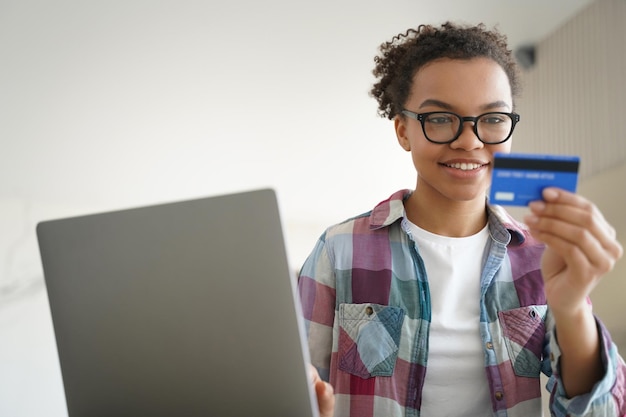 Adolescente de raça mista detém cartão de crédito usando serviços bancários on-line no laptop em casa E-commerce