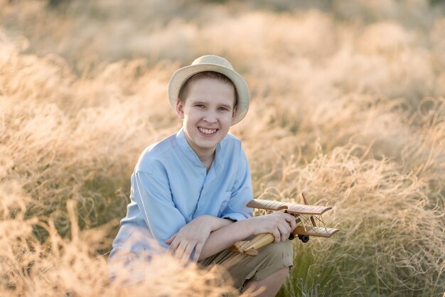 Adolescente de verão com modelo de avião sentado sorrindo na grama alta.