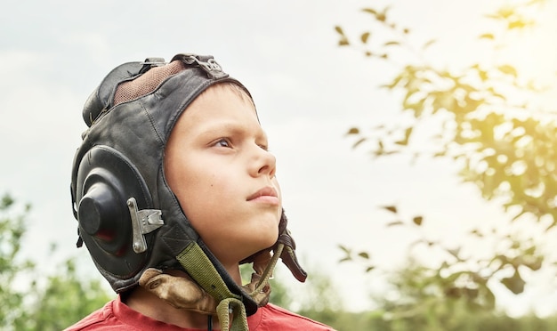 Un adolescente decisivo con casco piloto de cuero vintage mira hacia el cielo de pie en un parque verde