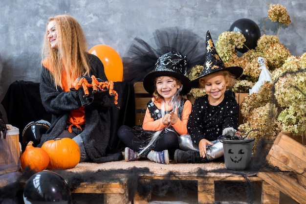 Adolescente entre decoración para la fiesta de Halloween con dos hermanas de 4-5 años se divierten en el fondo de decoraciones negras y naranjas, foto de humor