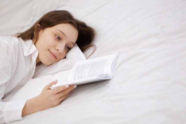 Adolescente deitada perto do livro na cama em seus sonhos do bem