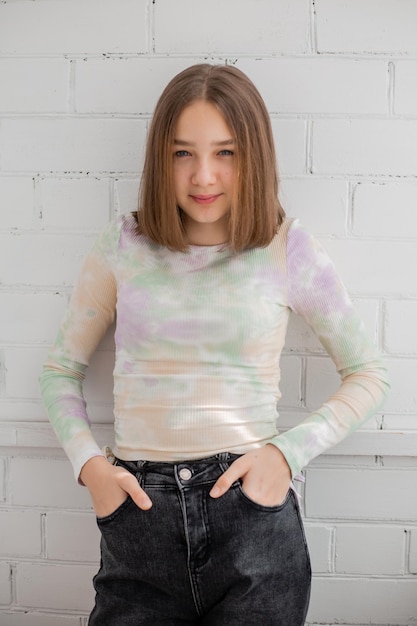 Una adolescente delgada con jeans y cuello alto posa contra una pared de ladrillo blanco. belleza natural, sin maquillaje, iluminación natural. espacio para texto. foto de alta calidad