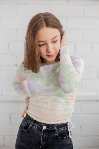 Una adolescente delgada con jeans y cuello alto posa contra una pared de ladrillo blanco. belleza natural, sin maquillaje, iluminación natural. espacio para texto. foto de alta calidad