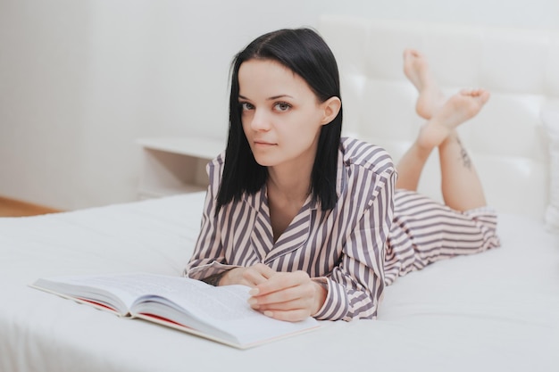 Adolescente descalça deitada na cama lendo um livro ou estudando