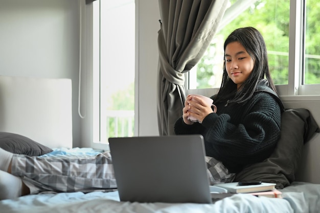 Adolescente despreocupada assistindo vídeo ou navegando em sites da Internet no laptop em seu quarto