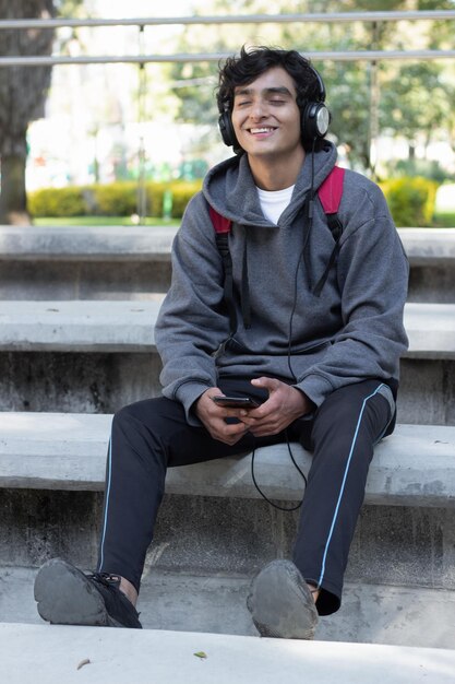 Adolescente despreocupado ouvindo música com fones de ouvido no parque, sorrindo e relaxado