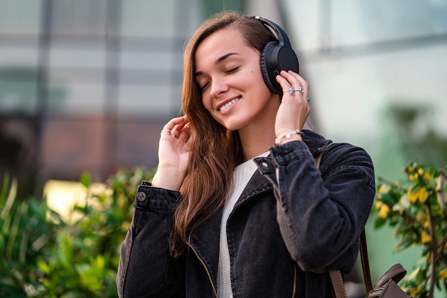 Adolescente disfruta y escucha música en auriculares inalámbricos negros mientras camina por la ciudad