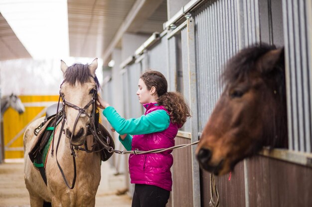 Una adolescente disfruta de un jinete que ajusta la montura y el equipo para la doma de caballos Jinete infancia Brida de animales ecuestres