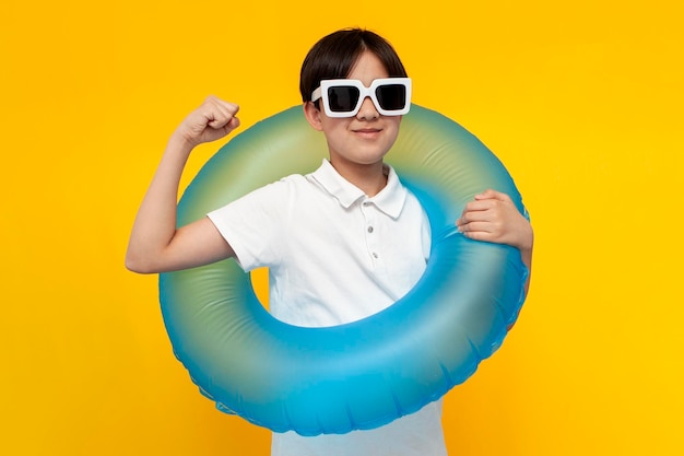 Foto un adolescente de doce años con gafas de sol sostiene un anillo de natación inflable y muestra gestos