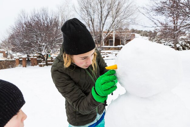 Adolescente e seu irmão mais novo construindo um boneco de neve em um jardim