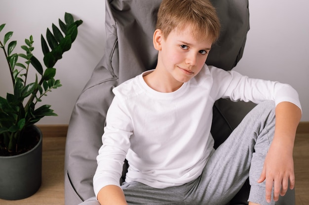 Adolescente elegante relaxado sentado em uma cadeira de saco de feijão em casa Maquete de camiseta branca