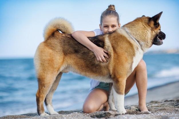 Adolescente em roupas leves abraça e adora cachorro amigo da raça Akita Inu na praia perto do Mar Negro em clima quente e ensolarado