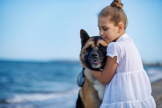 Adolescente em roupas leves abraça e adora cachorro amigo da raça Akita Inu na praia perto do Mar Negro em clima quente e ensolarado