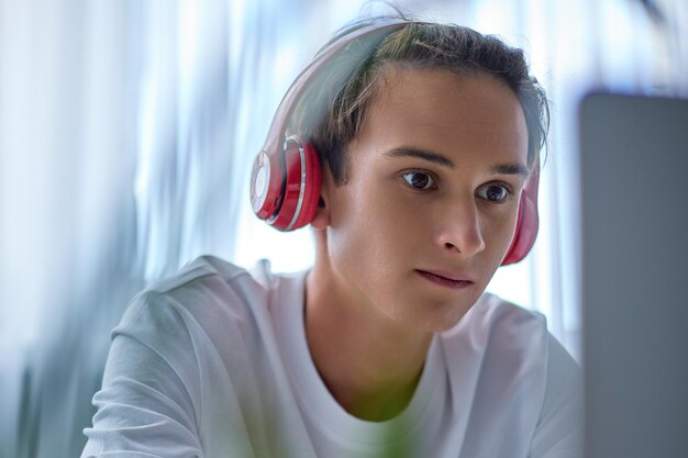 Adolescente em um par de fones de ouvido está olhando para um laptop