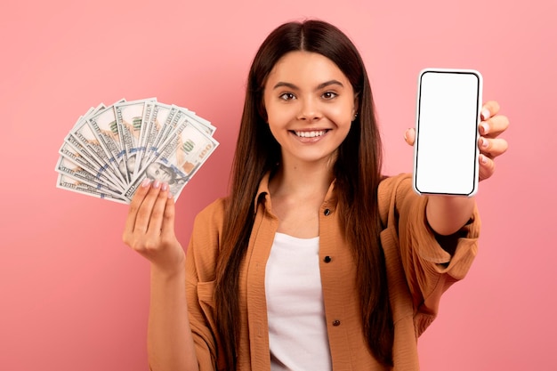 Foto una adolescente emocionada con la banca móvil que muestra un teléfono inteligente en blanco y tiene dinero en efectivo