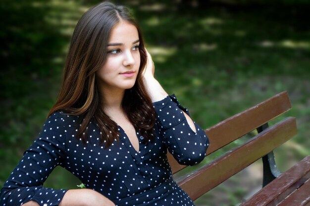 Adolescente emocional com tranças de penteado de cabelo comprido em uma camisa verde senta-se em um banco no parque