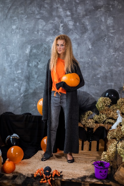 Adolescente entre a decoração para o feriado de Halloween, enorme abóbora na mão.