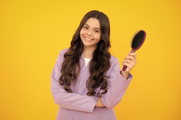 Adolescente escovando o cabelo com pente grande no fundo amarelo isolado do estúdio Menina adolescente com escova de cabelo Penteado para crianças Emoções positivas e sorridentes felizes da menina adolescente