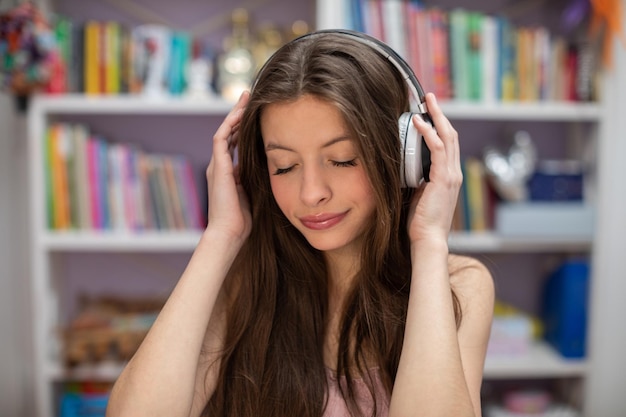Una adolescente escucha música con los ojos cerrados y una estantería con libros en el tel