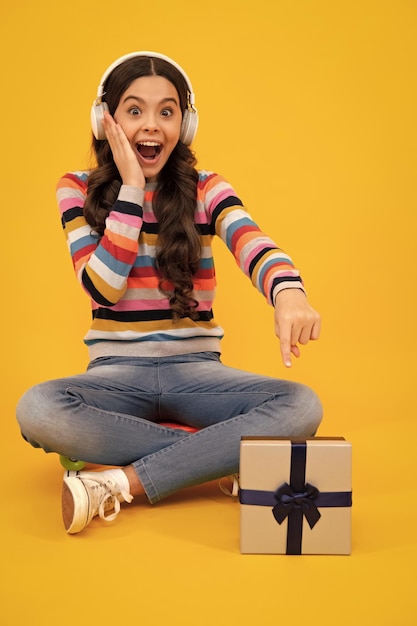 Adolescente espantado Criança adolescente segurando caixa de presente em fundo amarelo isolado Presente para aniversário de crianças Caixa de presente de Natal ou Ano Novo Menina adolescente animada