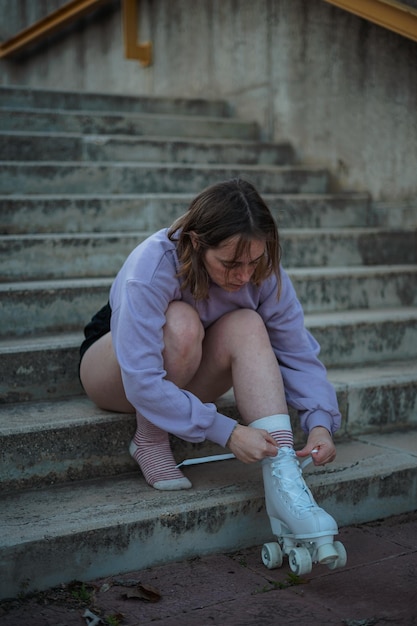 La adolescente está atando los cordones de los patines antes de practicar Está sentada en las escaleras