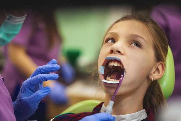 La adolescente está en el dentista. Ella se sienta en la silla del dentista y el dentista prepara los dientes para los aparatos ortopédicos.