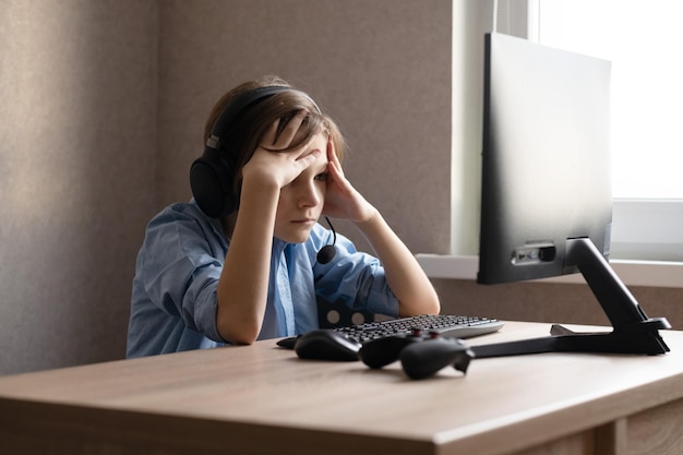 Un adolescente está sentado en casa frente a la computadora y jugando juegos de computadora en línea.