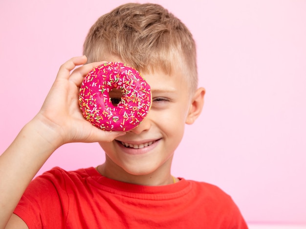 El adolescente se estaba divirtiendo con las donas mirándolas. un niño se divierte con donas sobre un fondo rosa. tiempo de diversión con la comida