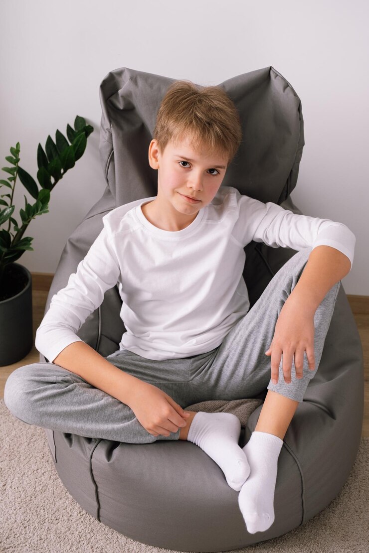 Foto adolescente con estilo relajado y rubio sentado en una silla de bolsa de frijoles en casa maqueta de camiseta blanca