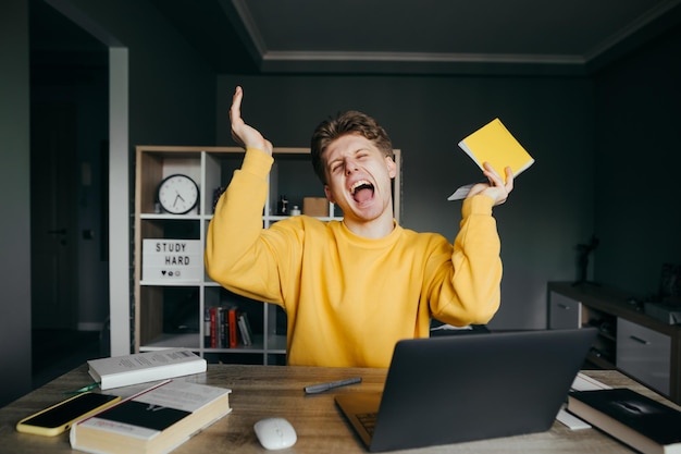 adolescente estudiando en casa en una mesa con una laptop y libros al fondo de una habitación acogedora