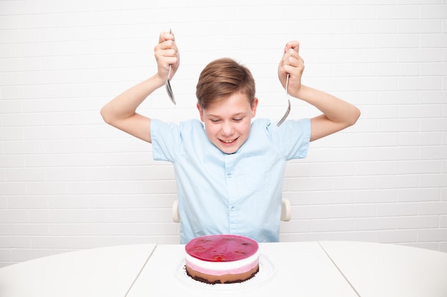 Adolescente europeo de fondo blanco con cubiertos quiere comer un pastel