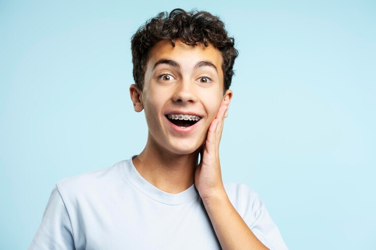 Foto adolescente excitado usando aparelhos dentários tocando o rosto olhando para a câmera isolada no fundo