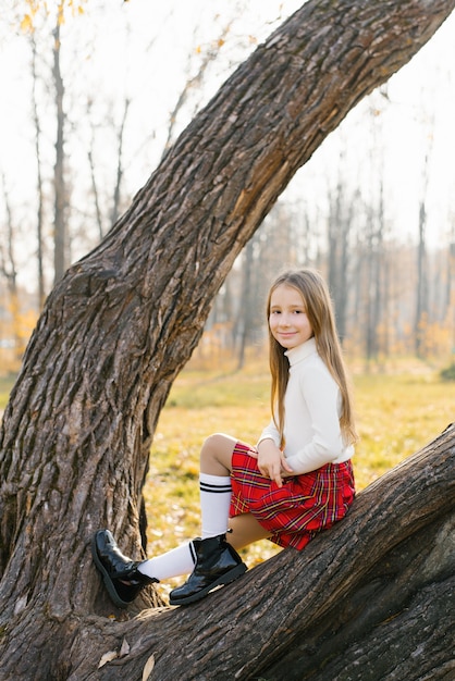 Una adolescente con una falda roja y un suéter blanco se sienta en un árbol