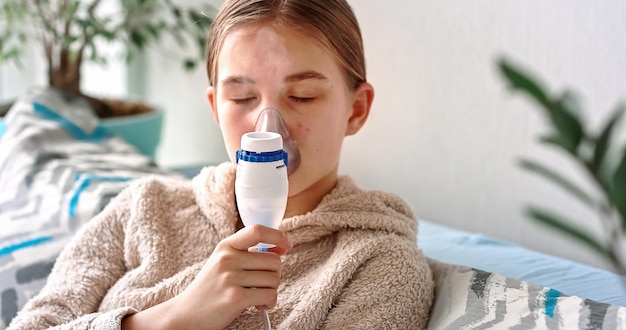 Adolescente faz inalação com um equipamento nebulizador. Criança doente segurando o inalador na mão e respira através de um inalador em casa