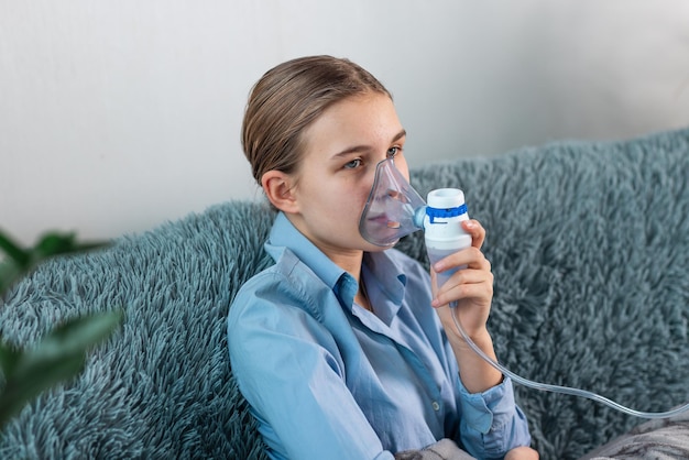 Adolescente faz inalação com um equipamento nebulizador. Criança doente segurando o inalador na mão e respira através de um inalador em casa