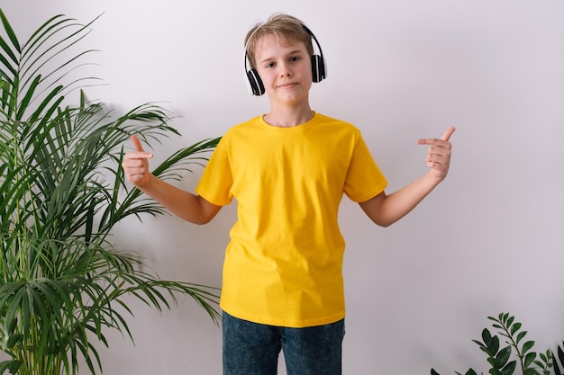 Adolescente feliz con auriculares apuntando a su camiseta Maqueta de camiseta amarilla