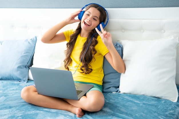 Un adolescente feliz con auriculares se relaja en la cama en casa escucha música usando una computadora portátil