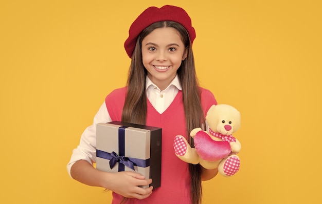 Una adolescente feliz con boina francesa sostiene un regalo de juguete y una caja de regalo sobre fondo amarillo el viernes negro