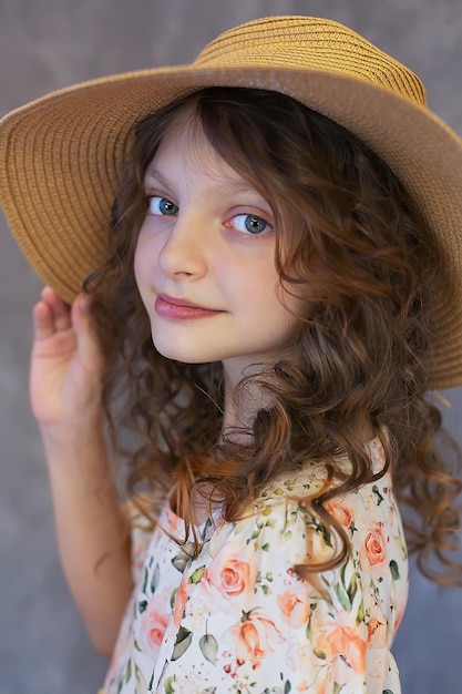 Una adolescente feliz con el cabello rizado y grandes ojos azules en un vestido de estampado floral y un sombrero de paja