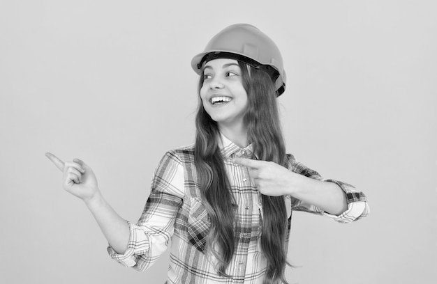 Una adolescente feliz con casco y camisa a cuadros señalando con el dedo el anuncio del espacio de copia