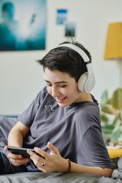 Adolescente feliz com fones de ouvido a olhar para o ecrã do smartphone